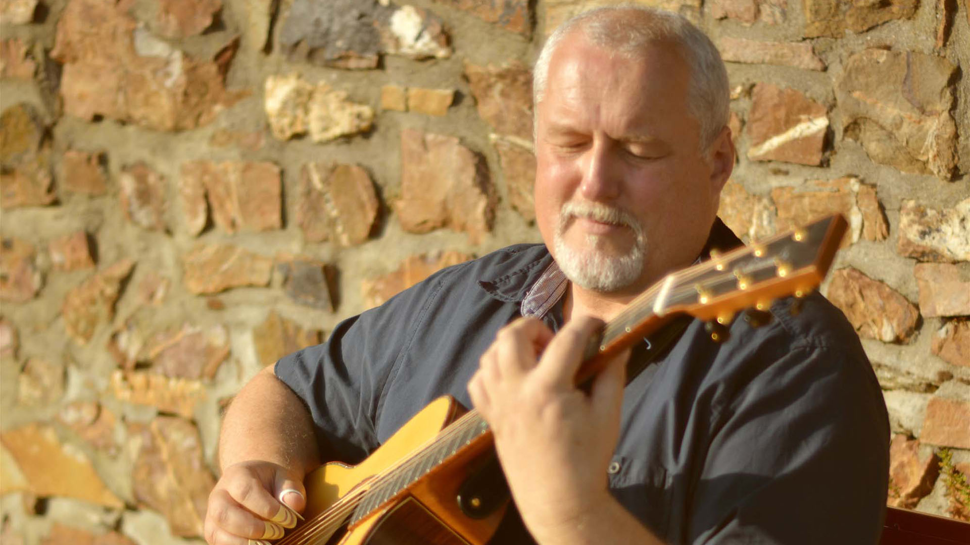 Peter Reimer mit Gitarre vor einer Mauer.