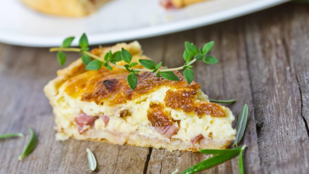 Quiches. Ein Stück Quiche Lorraine garniert mit Thymian und Rosmarin..