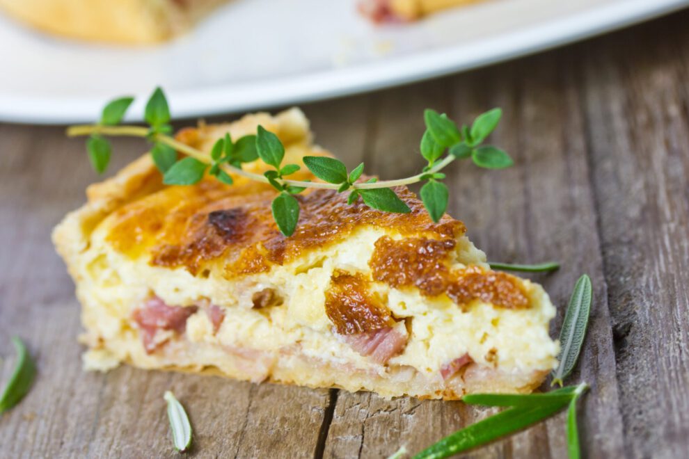 Quiches. Ein Stück Quiche Lorraine garniert mit Thymian und Rosmarin..